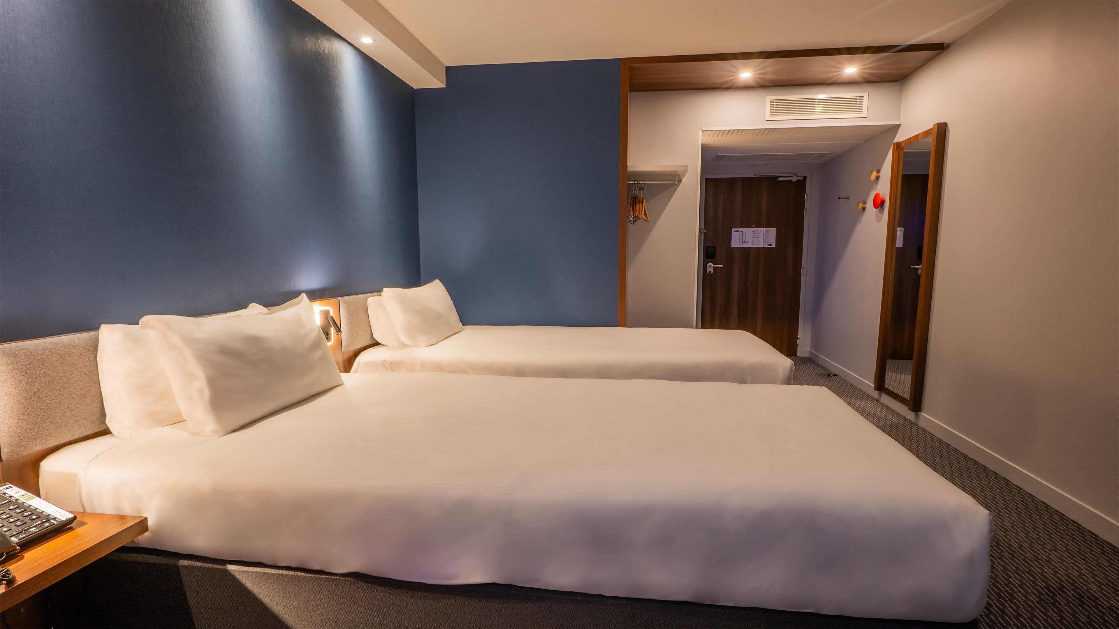Habitación de hotel con dos camas, un escritorio con una computadora portátil y un espejo.