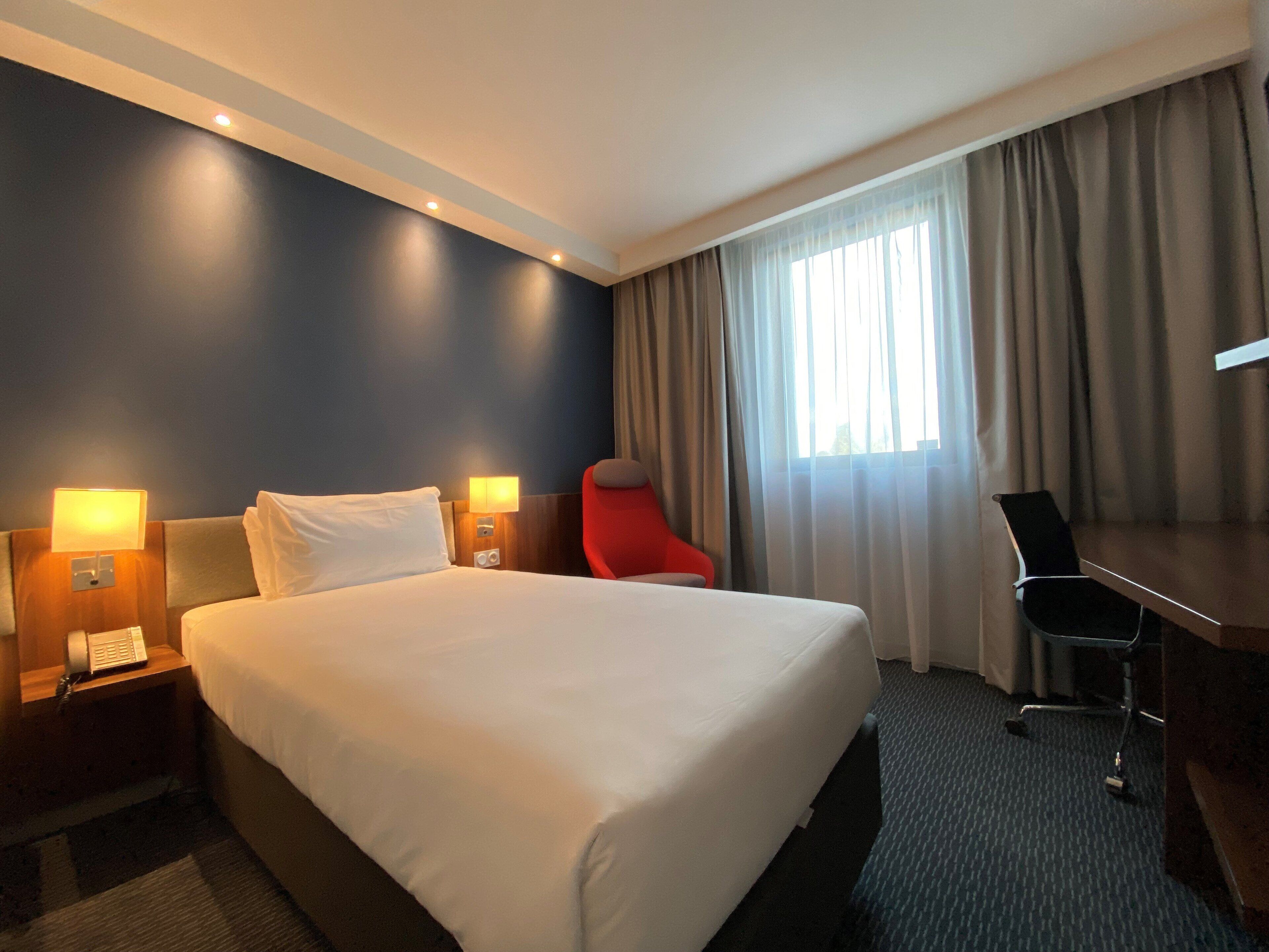 A hotel room with a large bed, bedside lamps, a desk, and a chair.