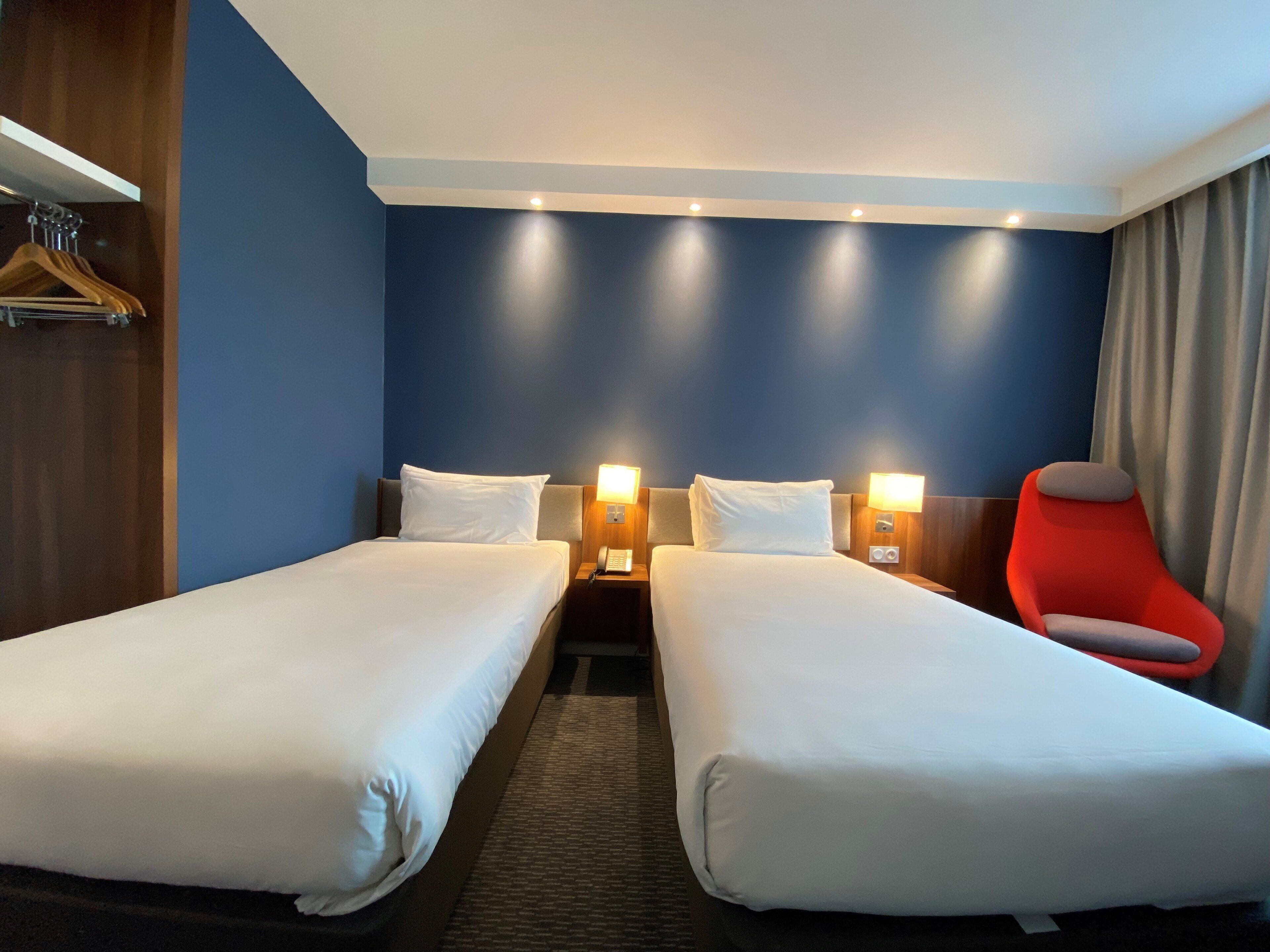 Habitación de hotel con dos camas individuales, una silla roja y un armario de madera.