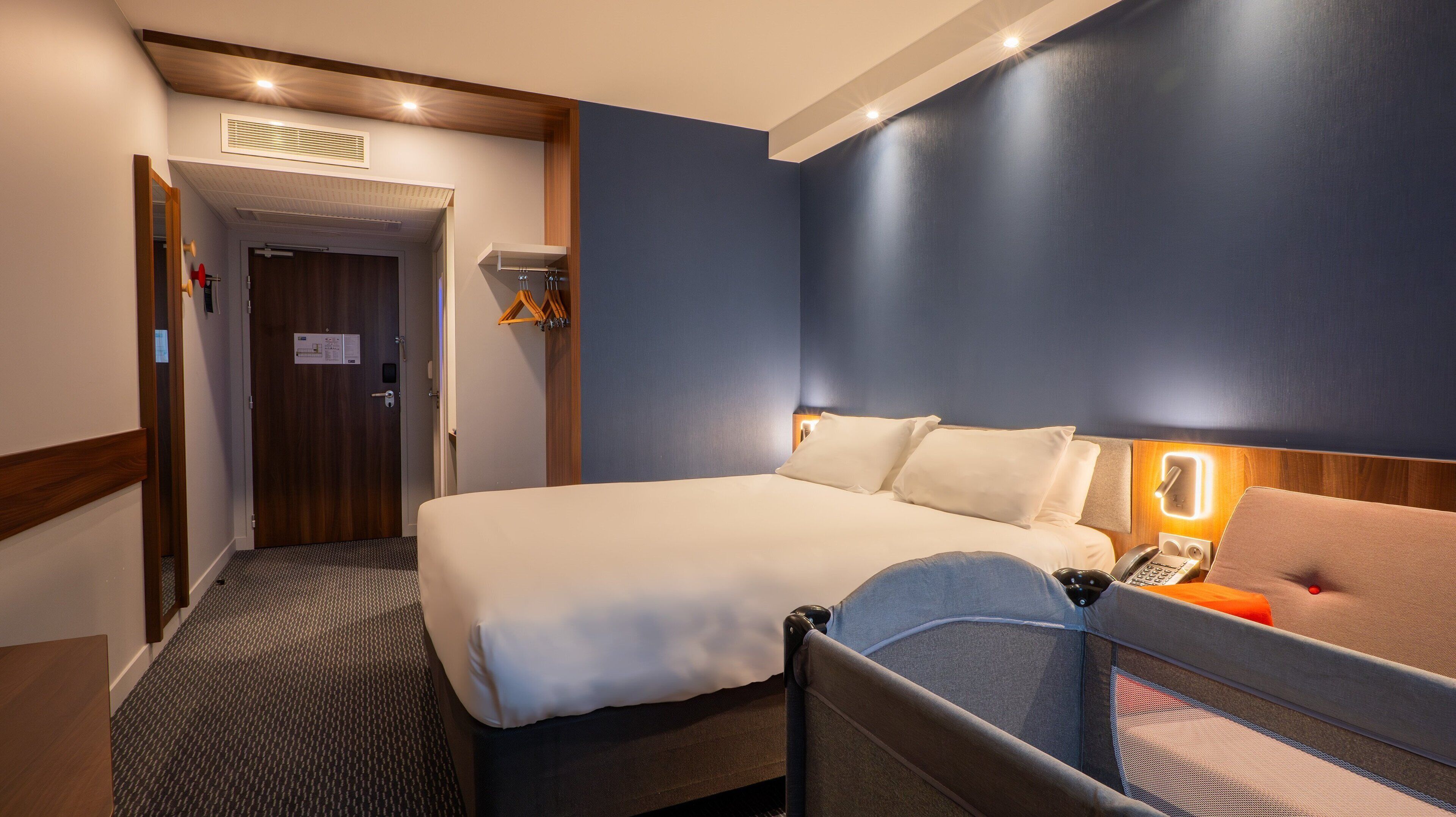 Een hotelkamer met een bed, een nachtkastje met lamp, een stoel en een kapstok.