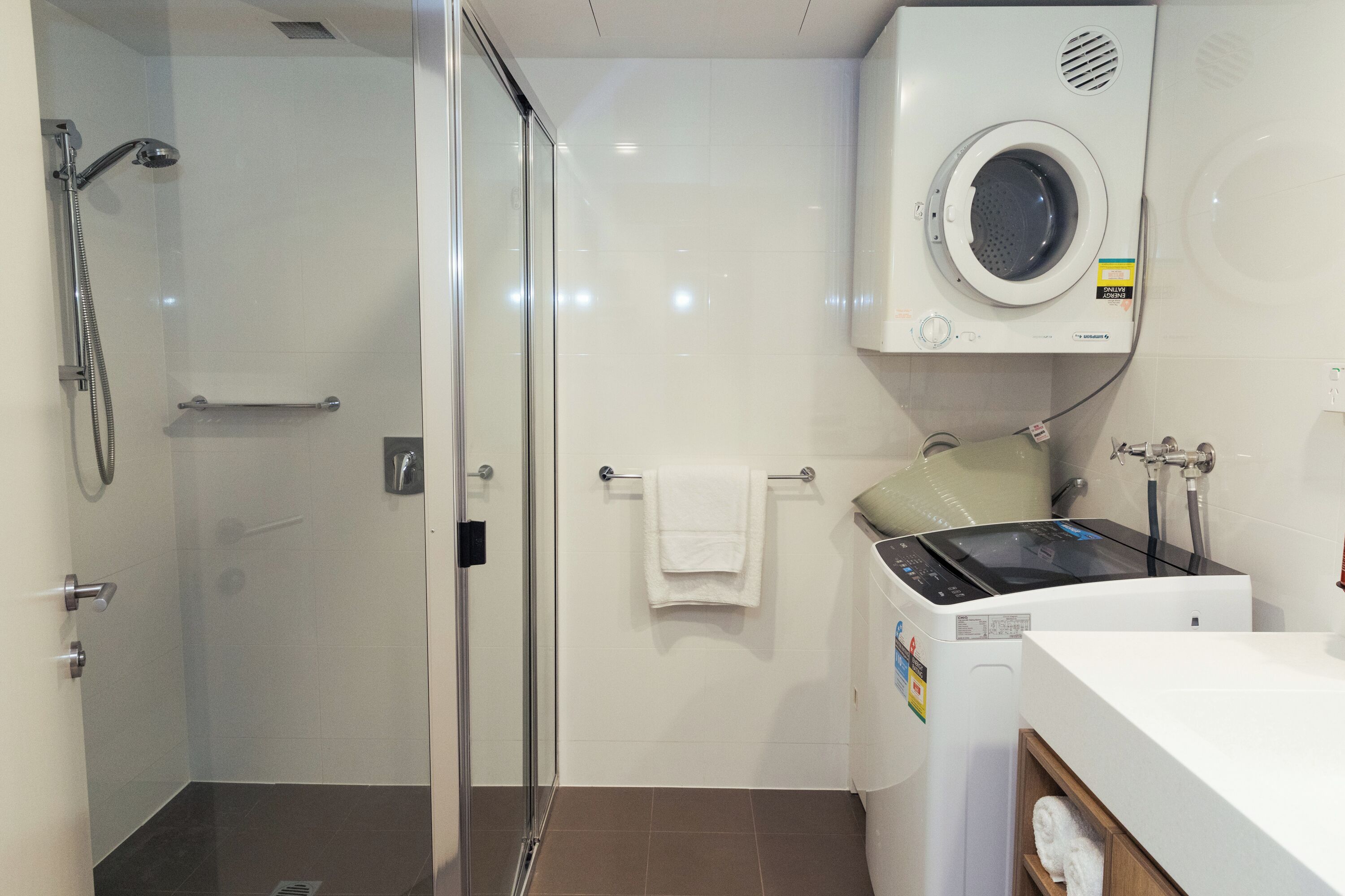 Ein modernes Badezimmer mit einer Duschkabine, einer integrierten Waschmaschine und einem Waschbecken mit Spiegel.