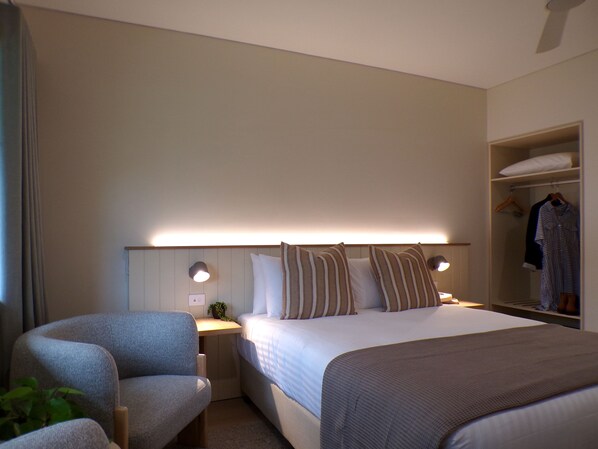 A hotel room with a bed, bedside tables, a chair, a wardrobe, and a nightstand with a lamp.