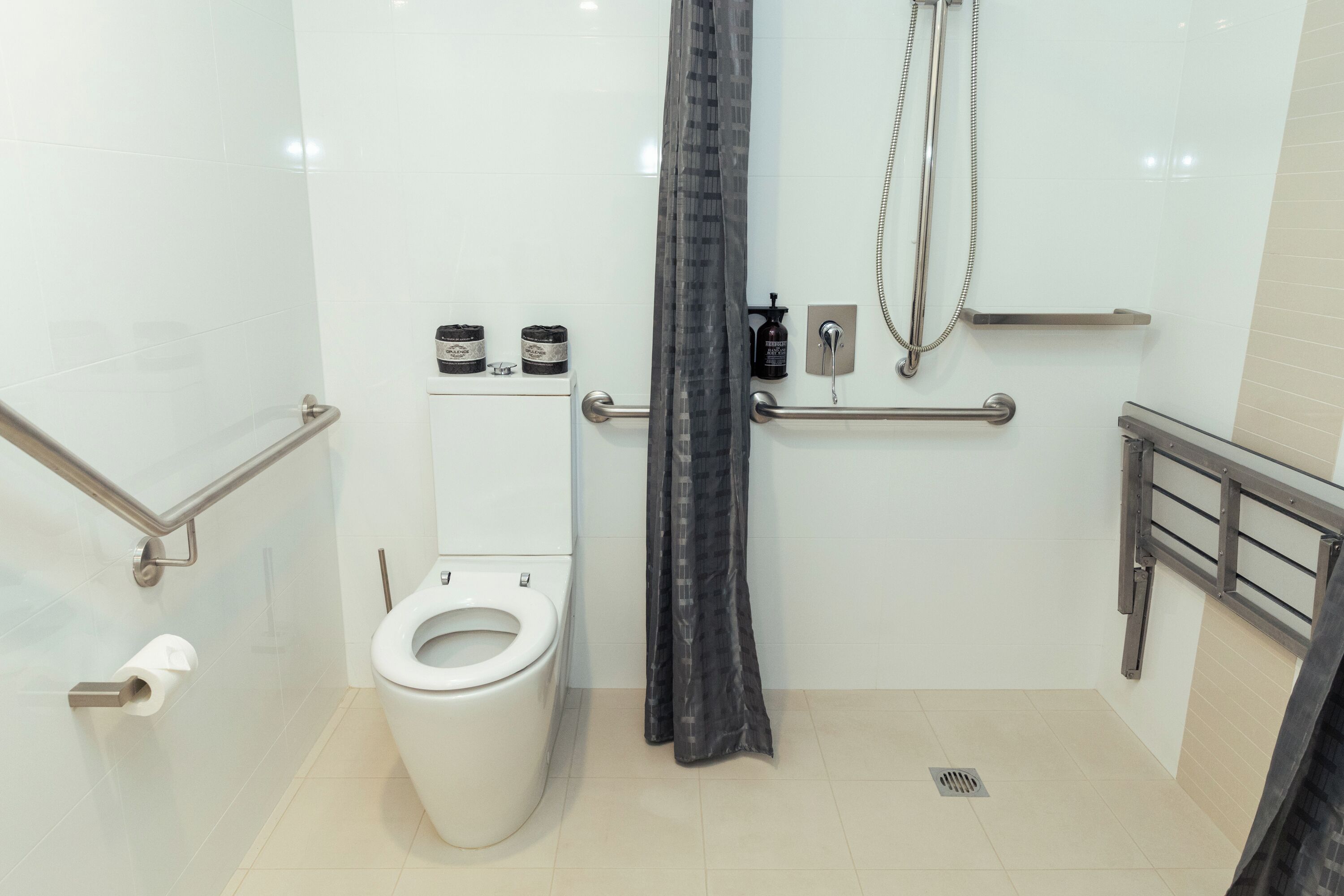 A modern bathroom with a white toilet, a shower with a handheld showerhead, and a grab bar.