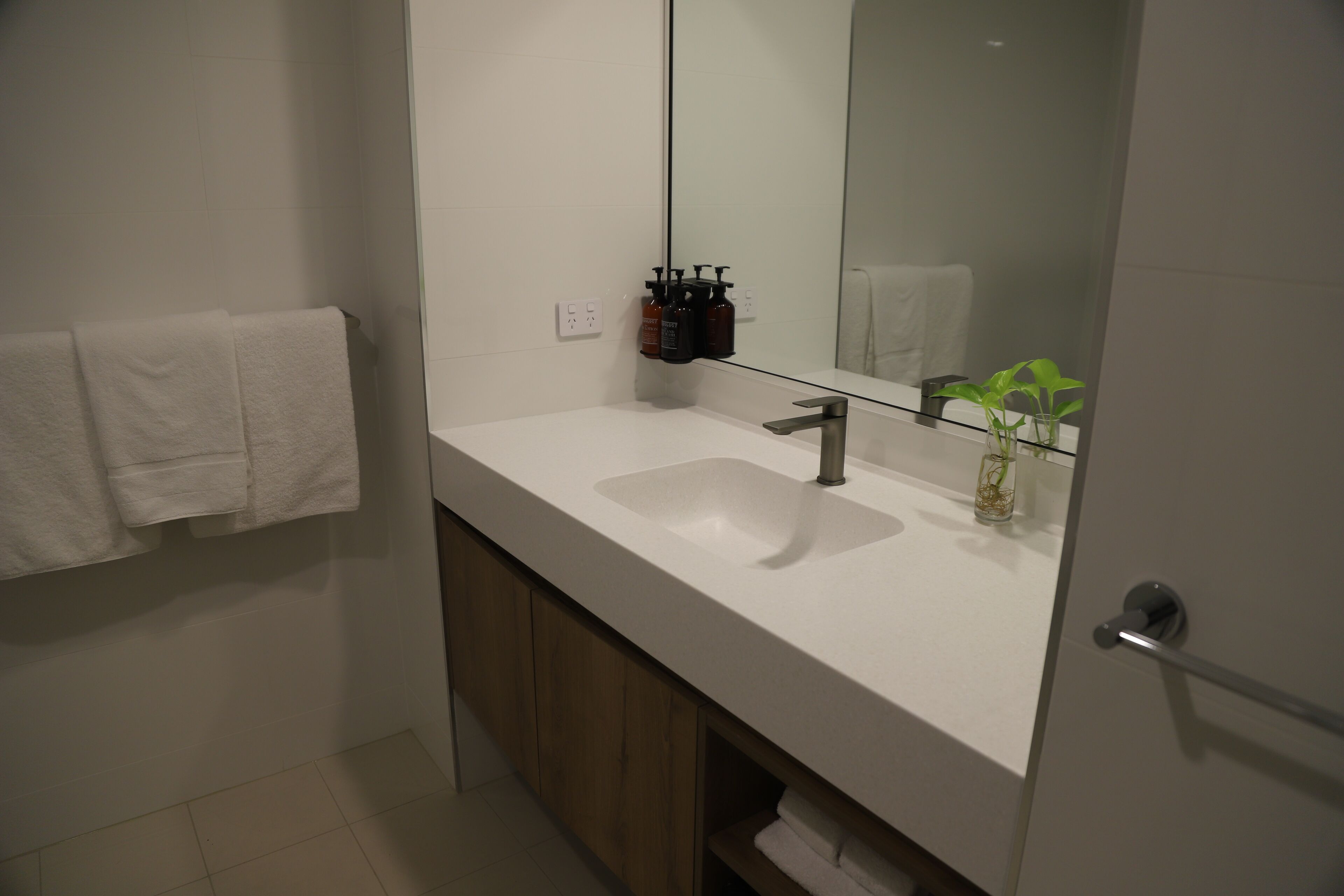 A modern bathroom with a white sink, a mirror, and a wooden cabinet.