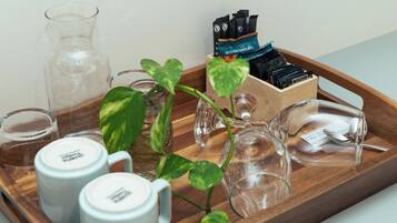 A tray with a glass pitcher, two white mugs, a glass carafe, a small glass, a wooden box with black and blue items, and a potted plant.