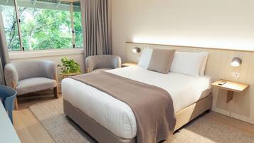 A modern hotel room with a large bed, two armchairs, a small table, and a window with curtains.