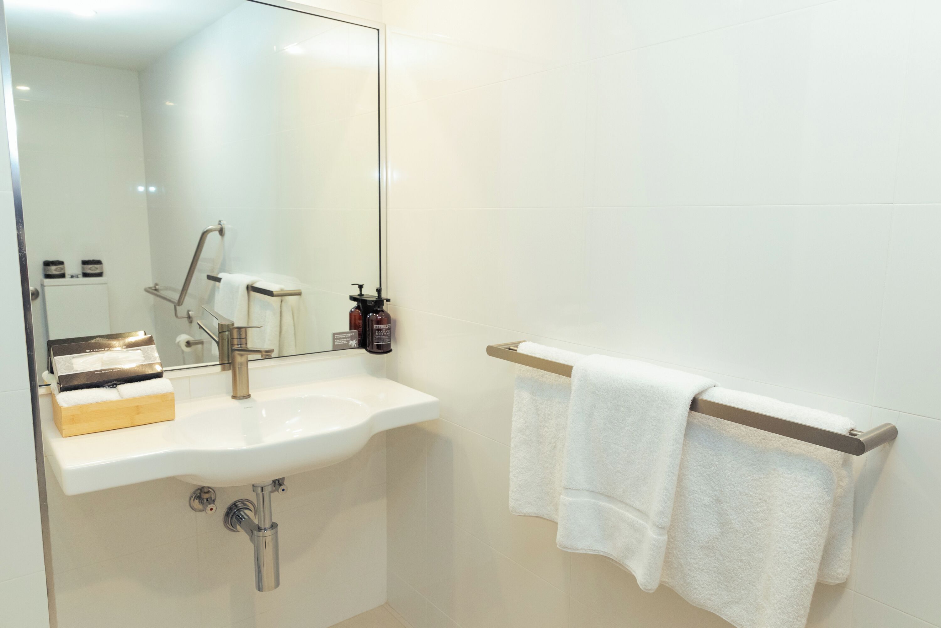 Une salle de bain moderne avec un lavabo blanc, un miroir et un porte-serviettes avec deux serviettes.
