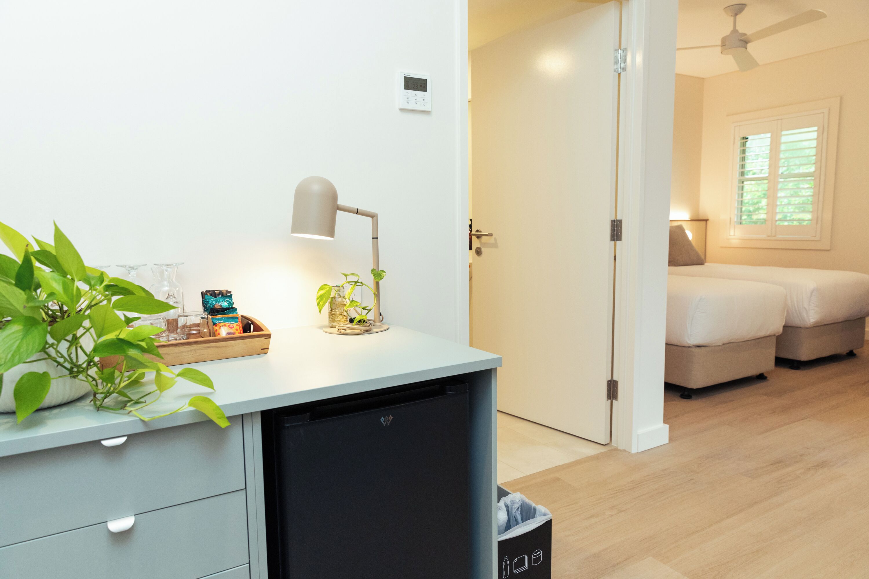 A modern bedroom with a bed, bedside table, and a desk with a lamp and plant.