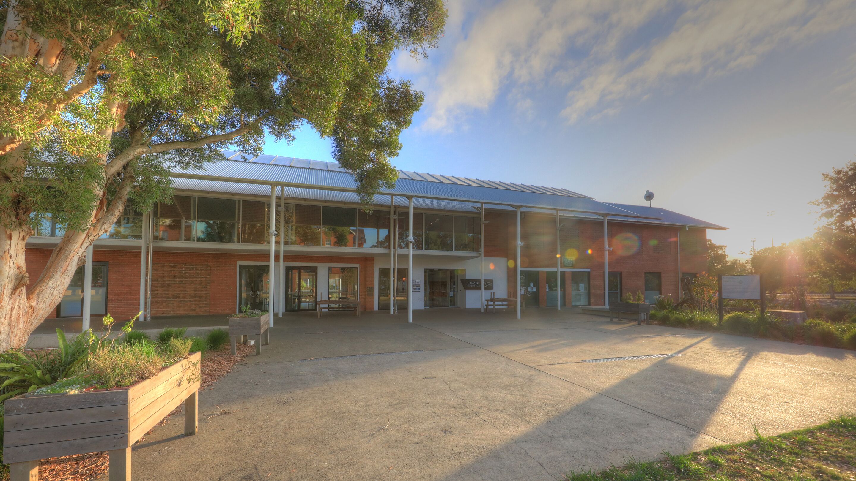 A two-story building with a glass facade, a brick exterior, and a covered outdoor area with benches.