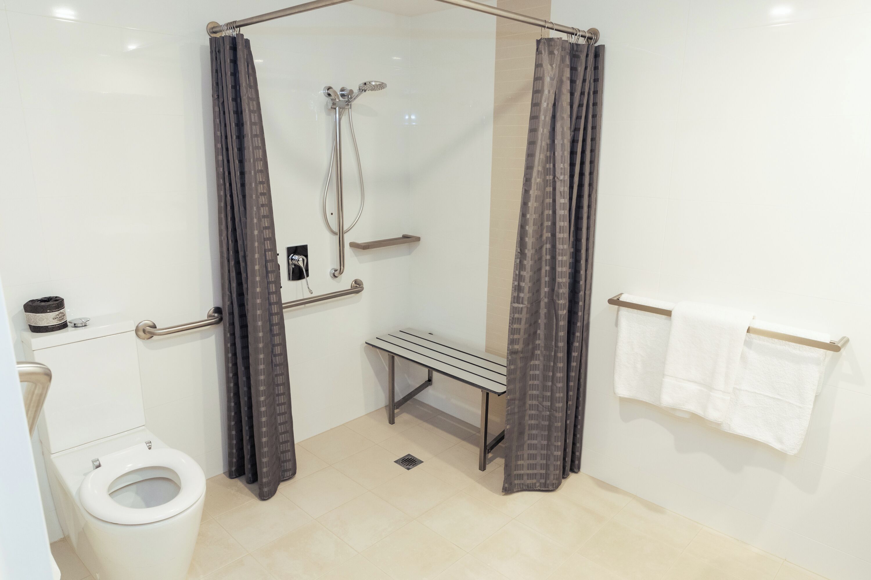 A modern bathroom with a shower, toilet, bench, and towel rack.