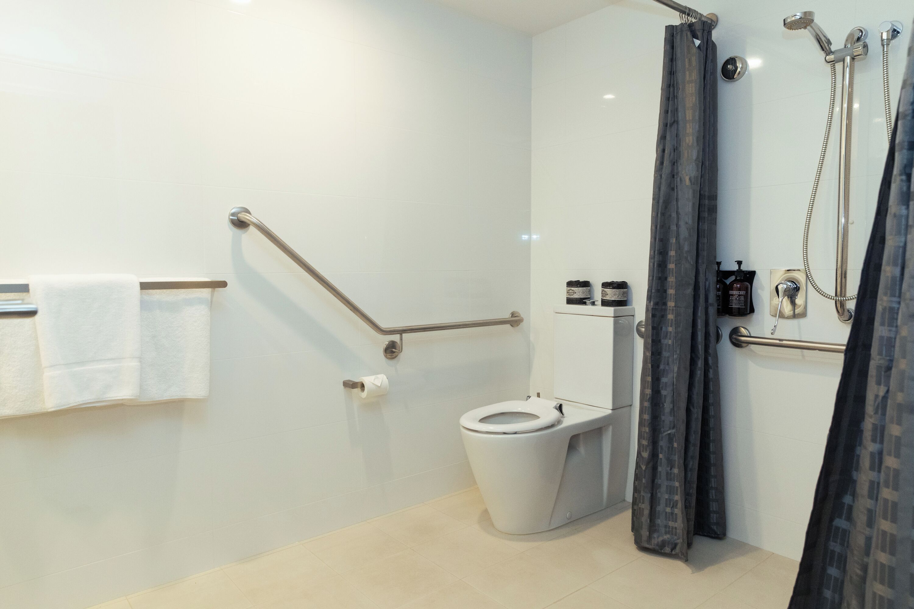 Un baño moderno con inodoro, barras de apoyo, ducha con cortina y un perchero para toallas.