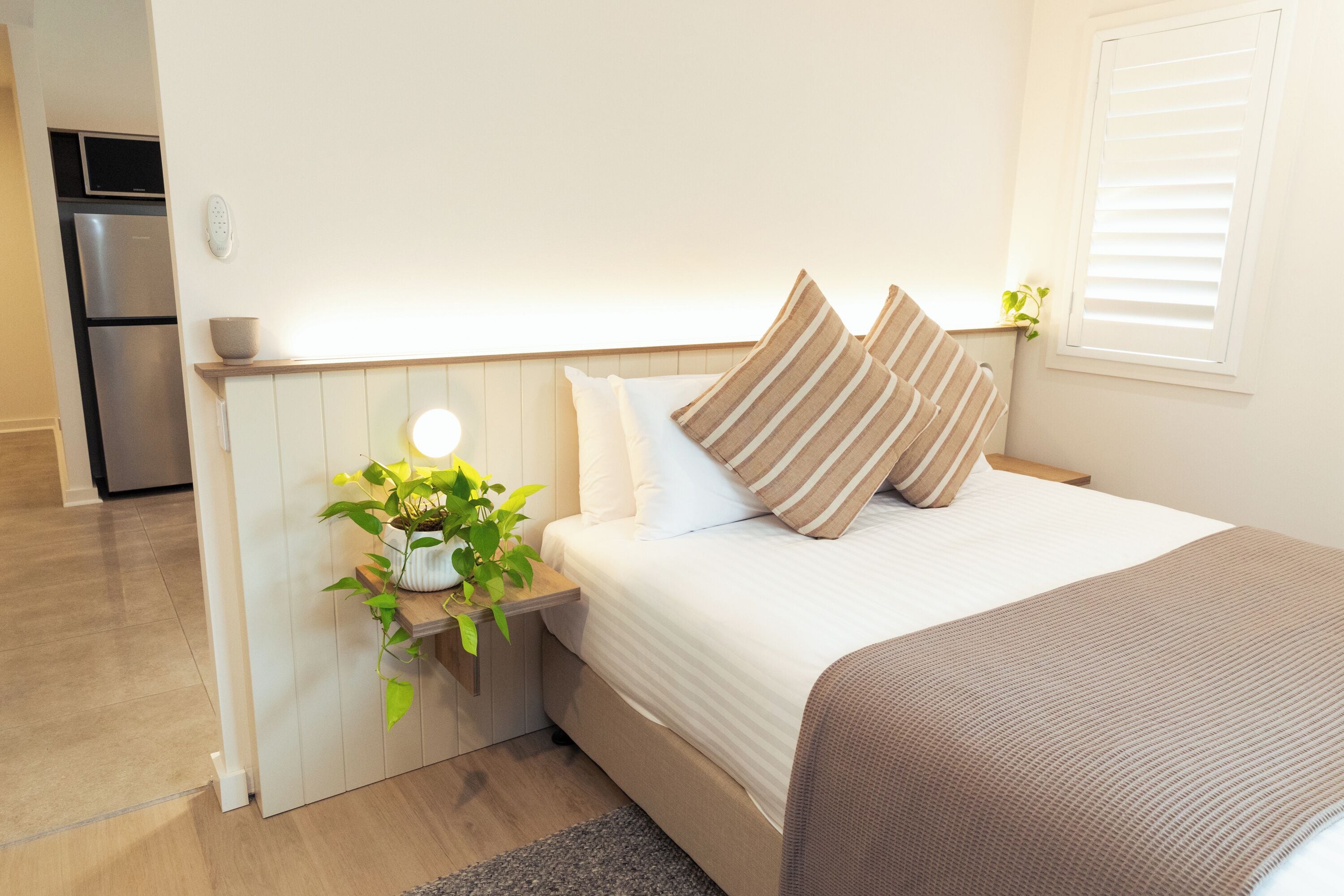 Un dormitorio ordenado con cama, mesita de noche y una planta pequeña.