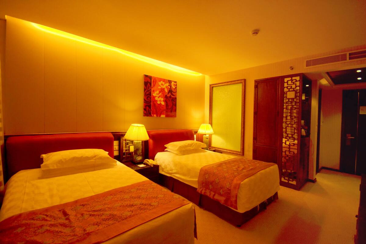 Habitación de hotel con dos camas, un cabecero rojo, un cuadro en la pared y un separador de madera.