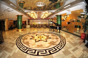 A grand lobby with a central floral floor design, a grand piano, and a high-ceiling with ornate chandeliers. - Beijing Olympic Park Boutique Hotel (Beijing)