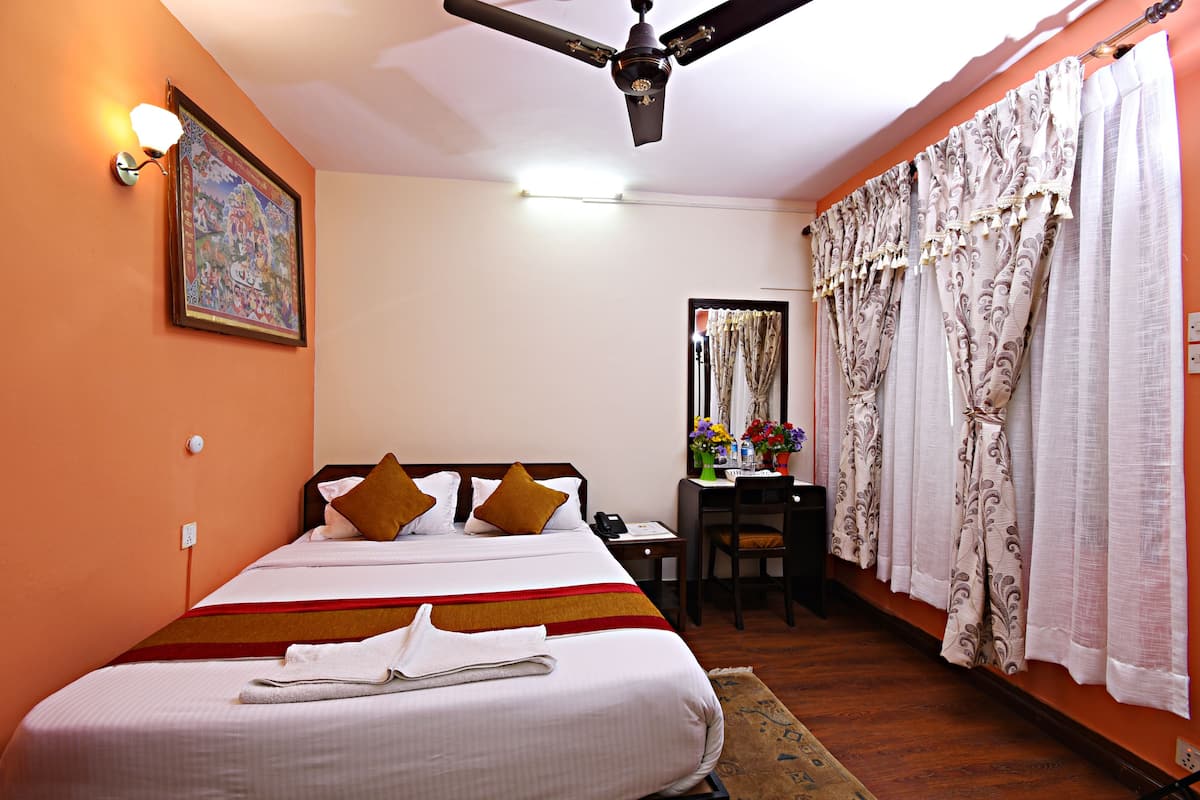 A hotel room with a bed, a desk, a chair, a ceiling fan, and curtains.