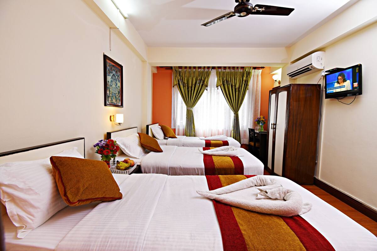 A hotel room with three beds, a television, an air conditioning unit, and a ceiling fan.