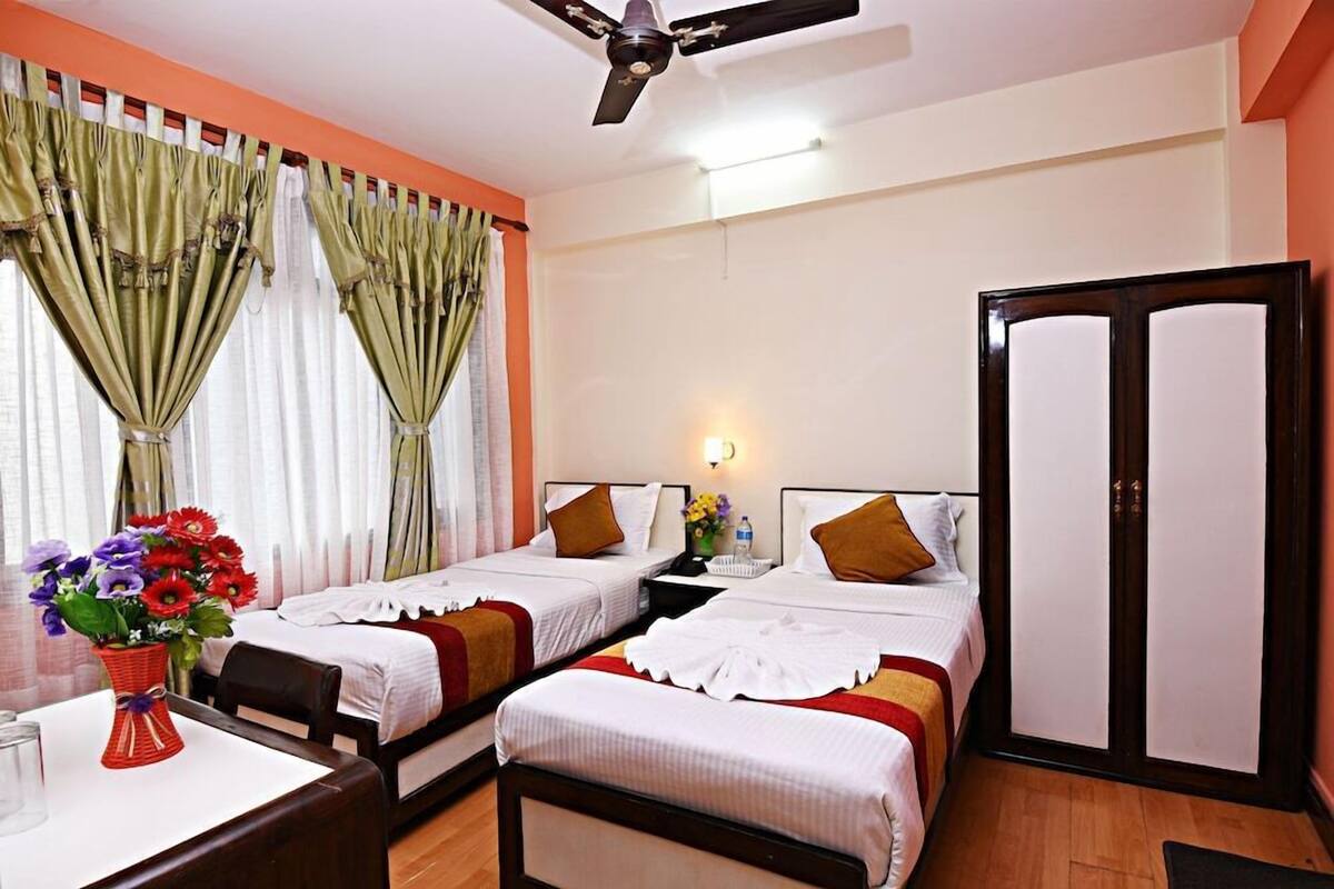 A hotel room with two beds, a desk, a chair, a ceiling fan, and a wardrobe.