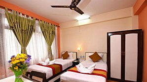 A hotel room with two single beds, a desk with a chair, a vase of flowers, and a wardrobe. - The Hotel Pleasure Home Inn (Kathmandu)