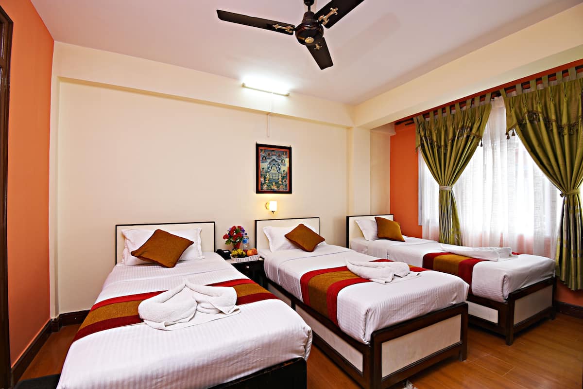 A hotel room with four single beds, a ceiling fan, a nightstand with a lamp, and a painting on the wall.
