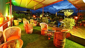 An outdoor seating area with wicker chairs and tables, surrounded by potted plants and a covered patio. - The Hotel Pleasure Home Inn (Kathmandu)