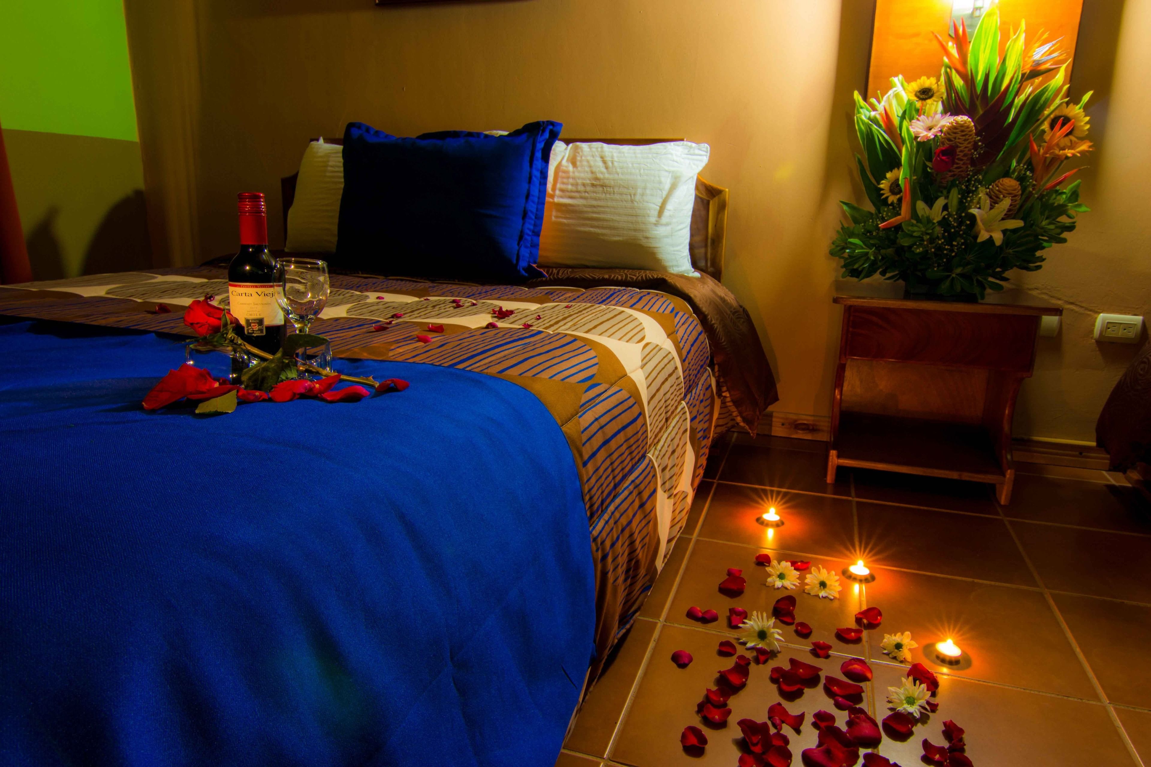 A hotel room with a bed, a bedside table with a vase of flowers, and a lit candle on the floor.