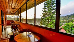 Un restaurante con mesas y sillas de madera, ventanas amplias que ofrecen vistas a zonas verdes y edificios.