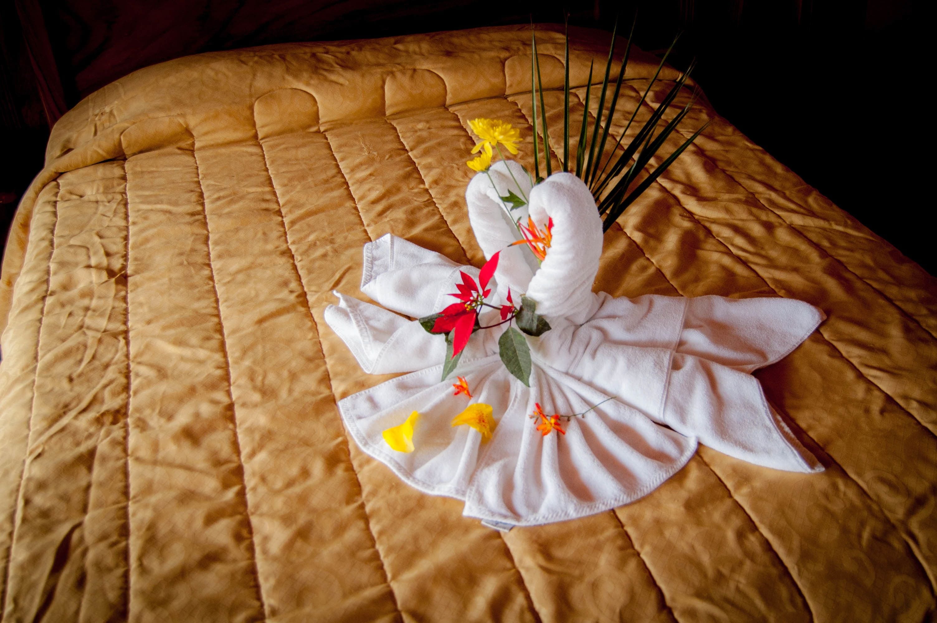 A bed with a golden quilted bedspread and a decorative arrangement of towels and flowers.