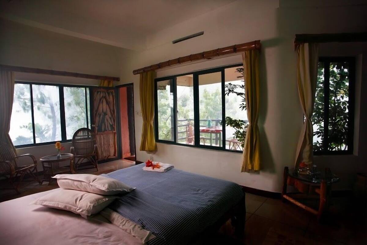 A room with a bed, two chairs, a small table, and large windows with curtains.