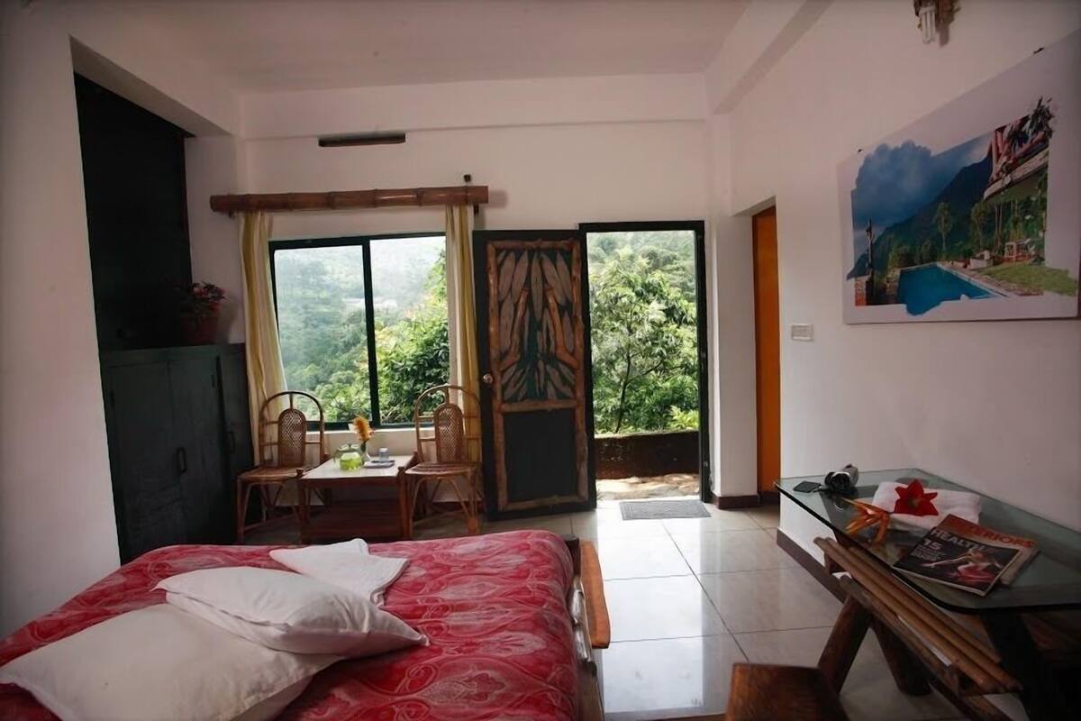 A bedroom with a bed, a desk, and a view of greenery through the door.