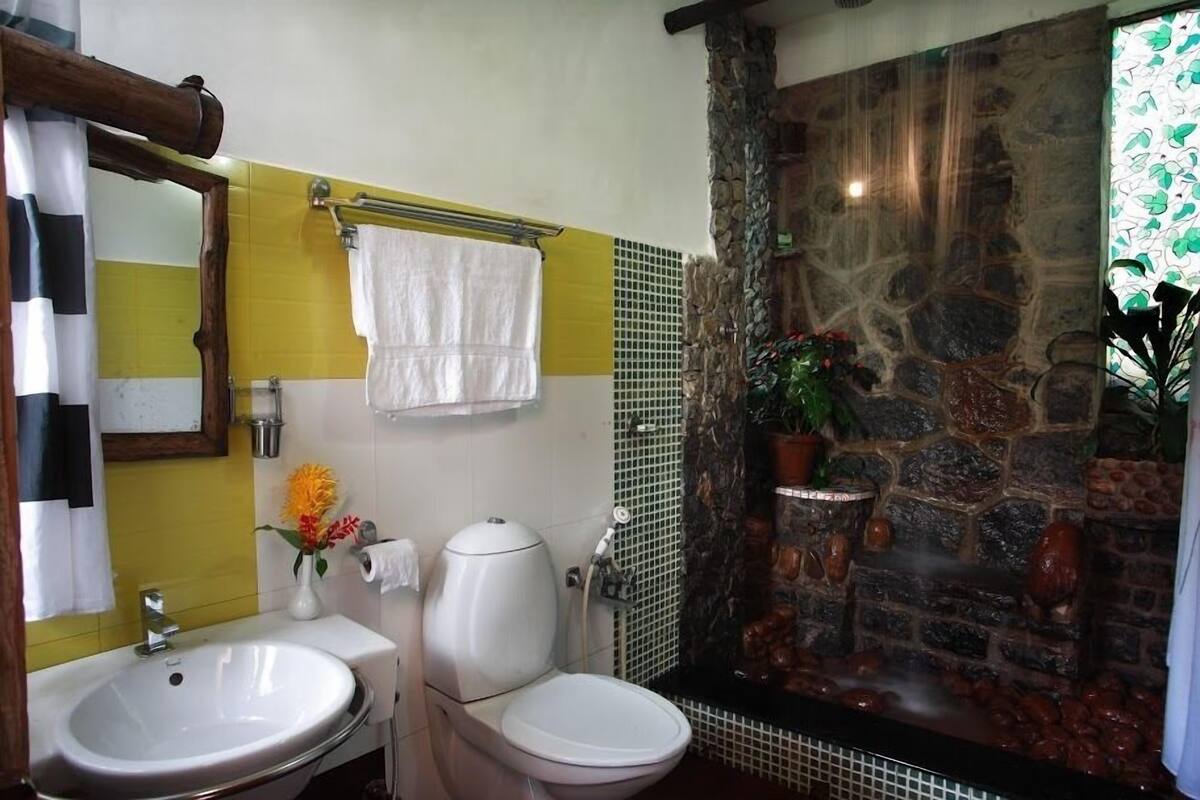 A bathroom with a white sink, a toilet, a mirror, and a stone wall with a water feature.