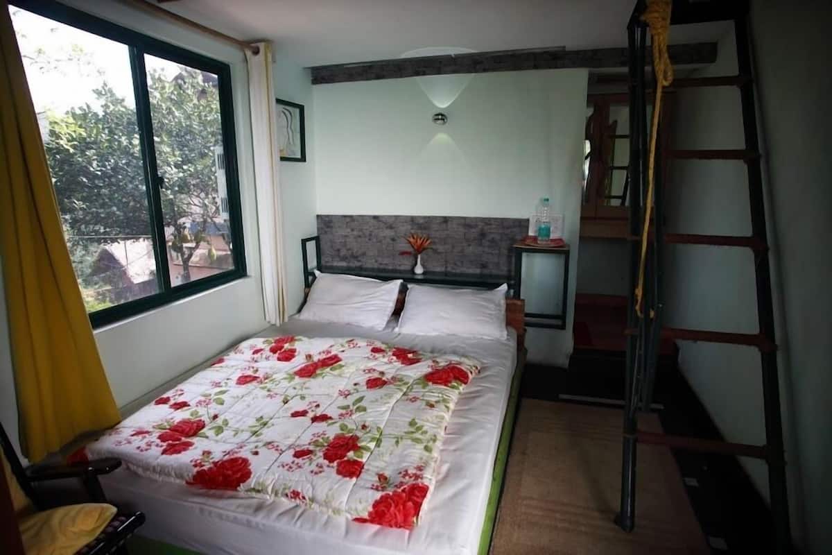 A bedroom with a bed, a nightstand, a ladder, and a window with curtains.