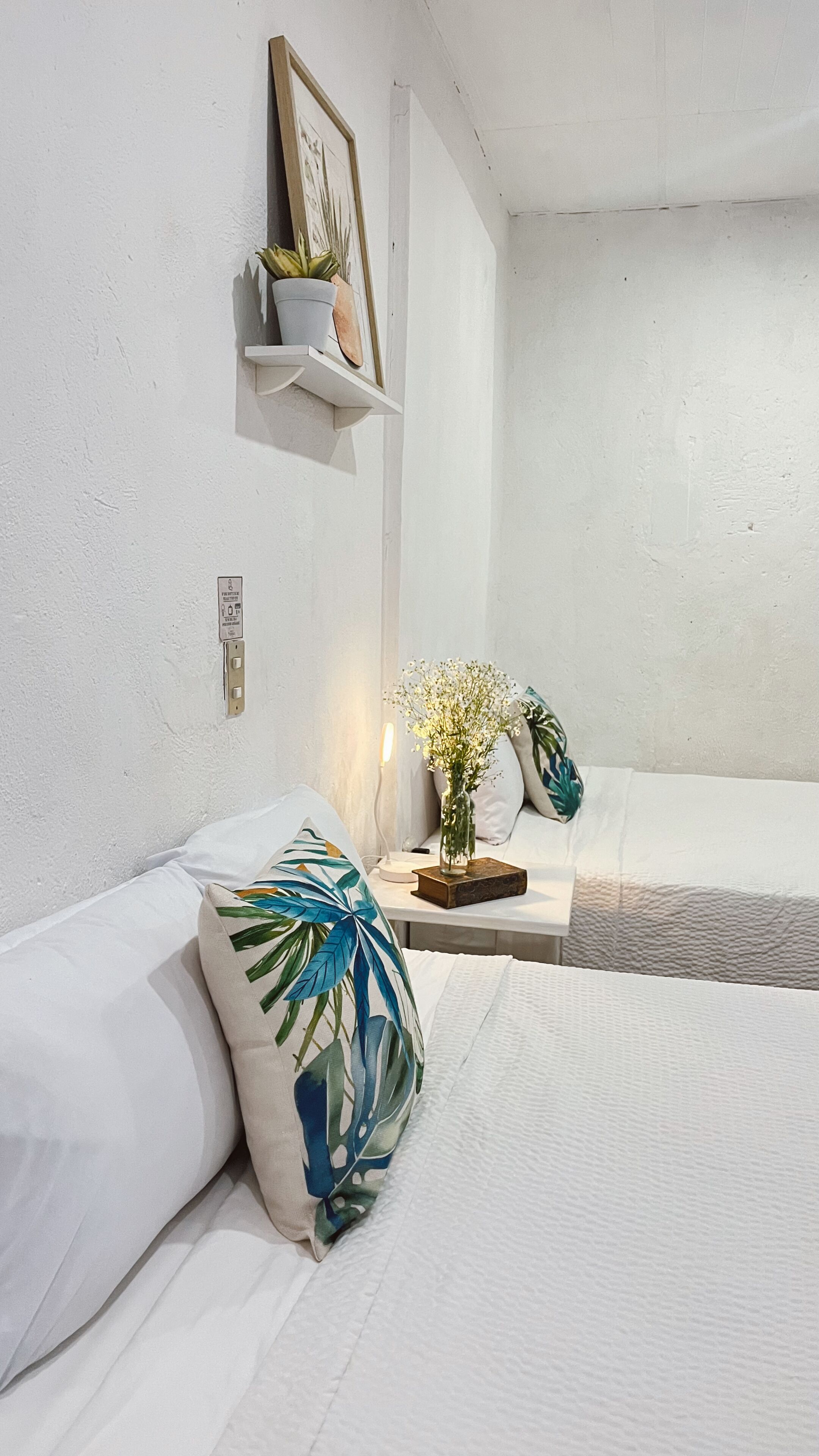 A minimalist bedroom with a bed, a bedside table with a vase of flowers, and a shelf with a plant.