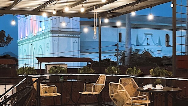 Un espace extérieur aménagé avec des chaises et une table en osier, sous un toit métallique agrémenté de luminaires suspendus.