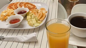 Un coin repas avec une table mise pour le petit-déjeuner, comprenant des crêpes, des œufs, des fruits et des boissons.