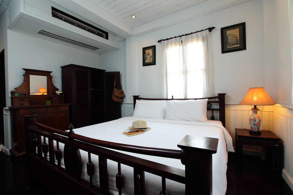 A neatly arranged bedroom with a wooden bed, a bedside table with a lamp, a dresser, and a mirror.
