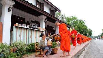 Une rangée de moines vêtus de robes orange, alignés devant un bâtiment à la façade blanche et aux volets en bois.