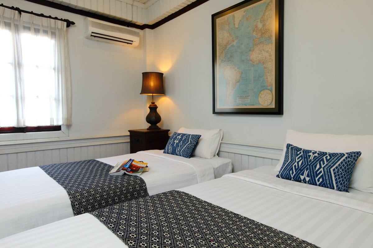 A hotel room with two beds, a map on the wall, a lamp, and a window with curtains.