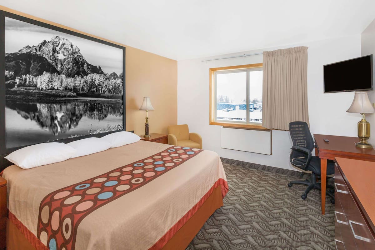 A hotel room with a bed, a desk, a chair, a TV, and a window with a view of a snowy landscape.