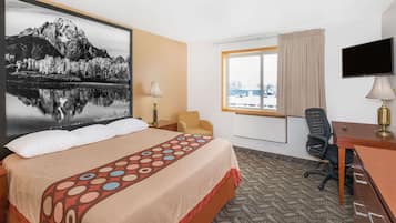 Habitación de hotel con cama, escritorio, silla, televisor y ventana con vista a un paisaje nevado.