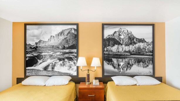 Een hotelkamer met twee bedden, een nachtkastje met een lamp, en twee grote ingelijste foto’s van bergen en een meer.