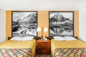 Habitación de hotel con dos camas, una mesita de noche con lámpara y dos cuadros grandes con paisajes de montañas y un lago.