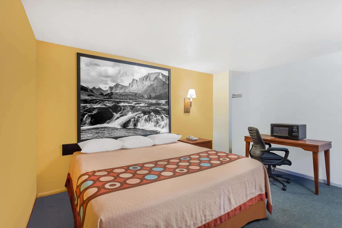 A hotel room with a bed, a desk with a chair, a lamp, and a radio.