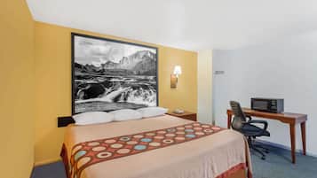 A hotel room with a bed, a desk with a chair, a lamp, and a radio.