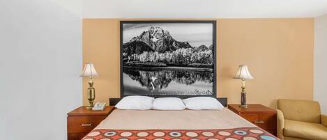 Une chambre d’hôtel avec un lit, deux lampes de chevet, une chaise et un tableau encadré au mur.