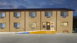 Een meerlaags hotel met een plat dak, meerdere ramen en een parkeerplaats met aangegeven parkeerplaatsen.