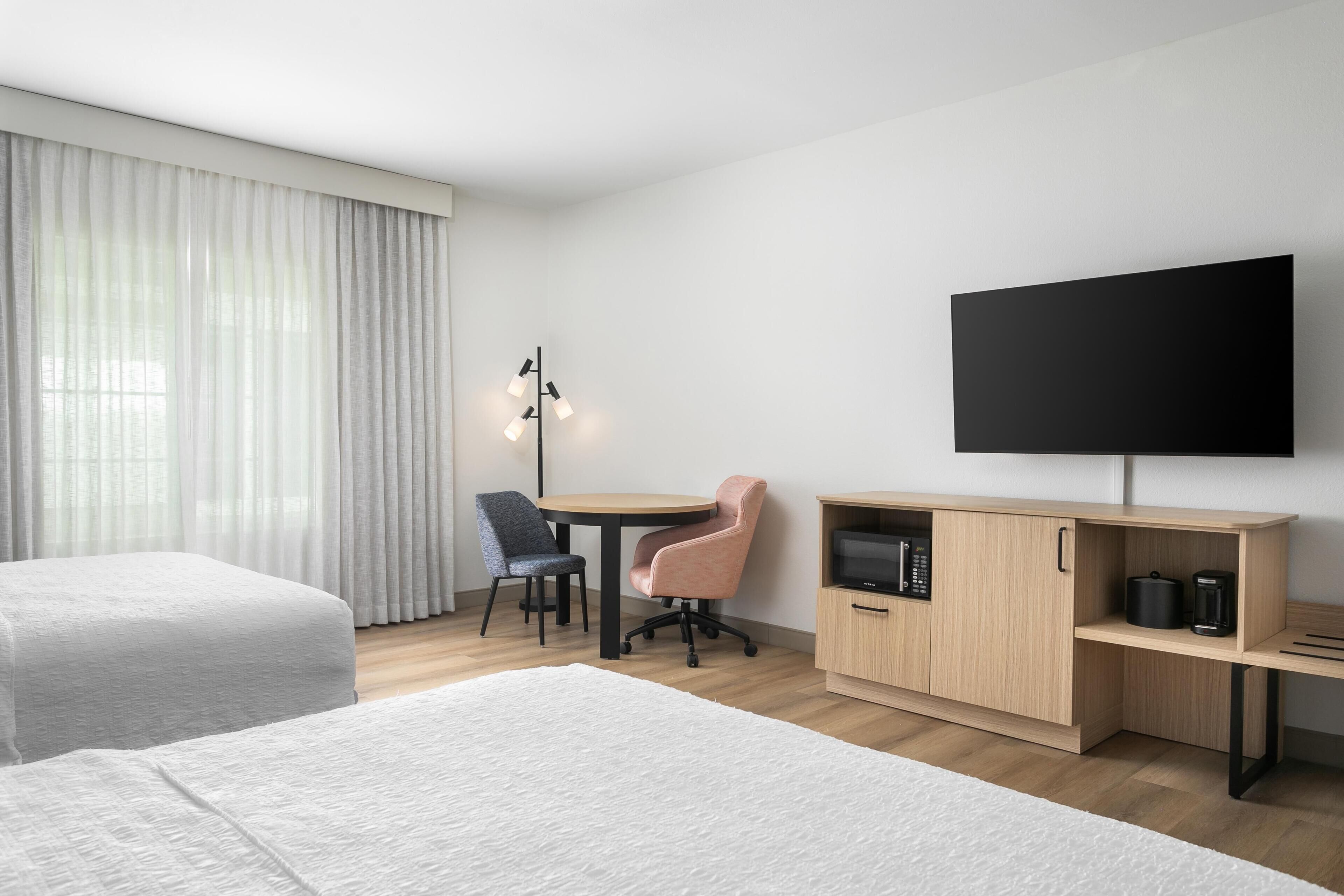 A hotel room with two beds, a desk, a chair, a TV, and a coffee machine.
