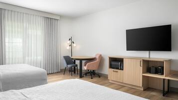 A hotel room with two beds, a desk, a chair, a TV, and a coffee machine.