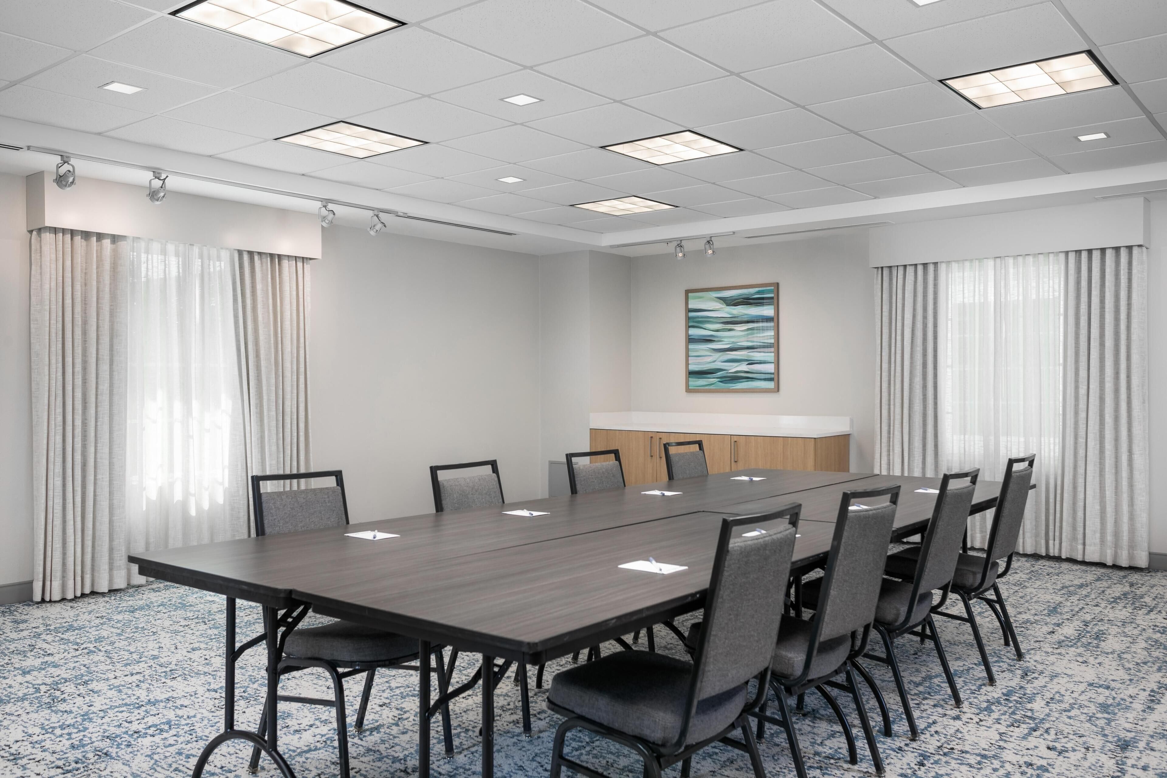 A conference room with a long table, chairs, a whiteboard, and a painting on the wall.