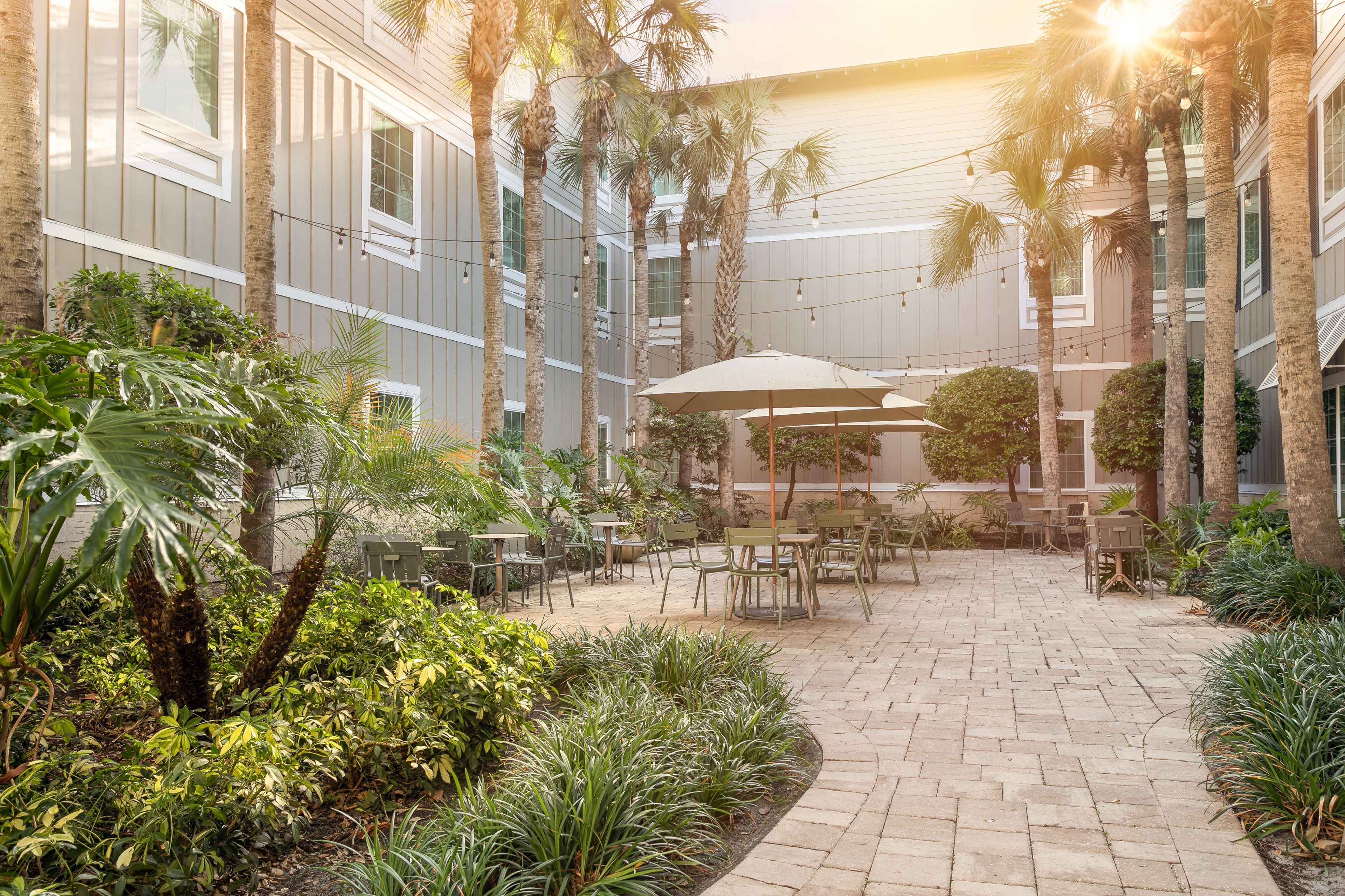 A courtyard with outdoor seating, palm trees, and a building with vertical siding.