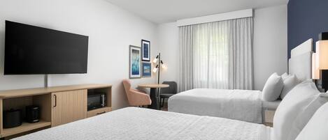 A hotel room with two beds, a flat-screen TV, a desk with a coffee maker, a chair, and a window with curtains.